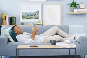 Smiling man relaxing on couch using a smartphone