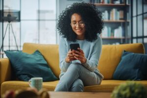 woman grinning while looking at mobile phone on couch