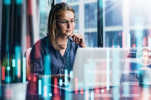 Young woman looking at her computer with stock market graphs overlaying the scene