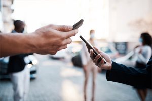 Two different hands holding up two different mobile phones in an urban city environment