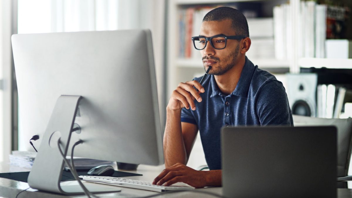 Man holding pen to chin while looking at computer monitor