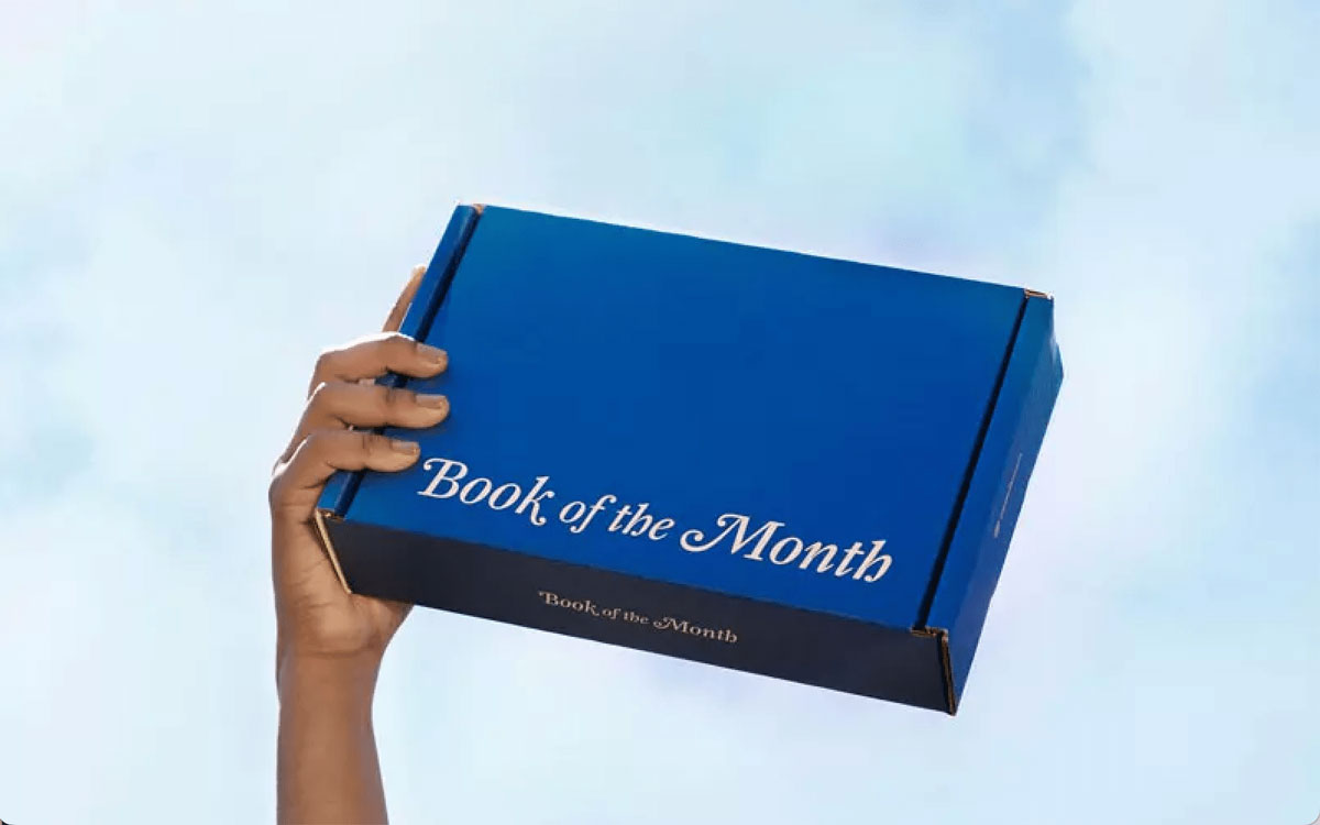 Hand holding book of the month shipped box against blue sky