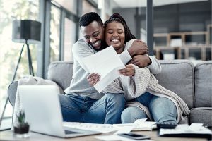 Excited couple hugging while looking at papers and sitting on the couch