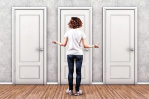 Woman standing before 3 doors, holding shoulders in a shrugging position