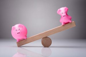 Wooden Seesaw with 2 piggy banks, and 1 piggy bank has been squeezed until its skinny