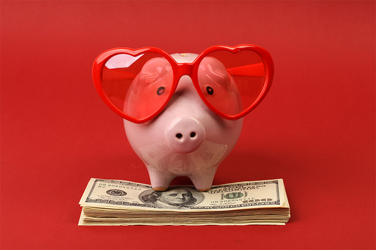 piggy bank with heart sunglasses standing on top of a stack of cash