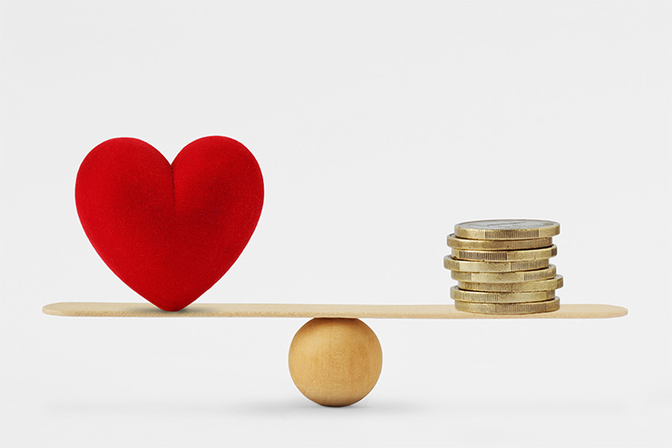 seesaw equally balancing a red plush heart versus a stack of coins