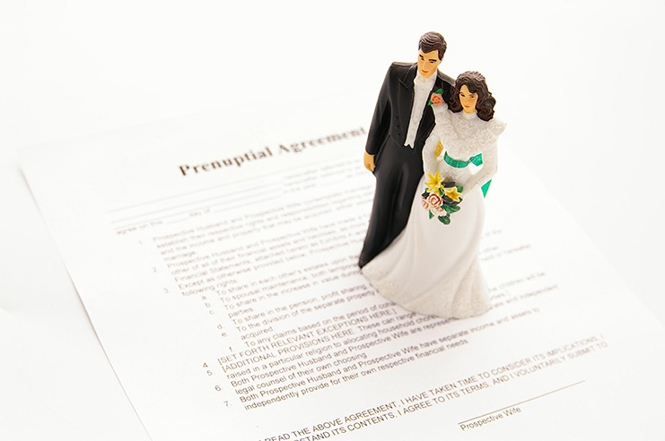 toy married couple standing on top of prenuptial paperwork