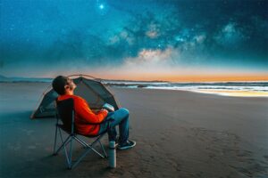 Man sitting alone near his beach campsite under the night sky