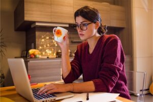 Woman working on laptop while holding mug