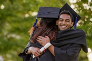 Young man in graduation cap and gown hugging classmate