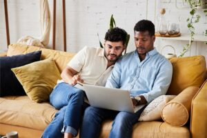 Young male couple looking at a laptop together while sitting on a couch