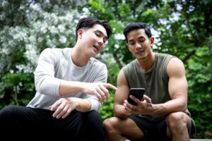 Two young men looking at mobile phone together while sitting outside
