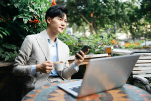 Young man wearing white coat holding coffee front laptop
