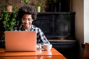 African man in glasses using laptop while sitting at restaurant, concept of young people working