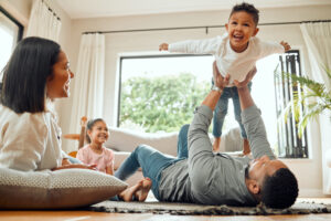 A happy family together in a bright living room. A father holds his laughing son in the air.