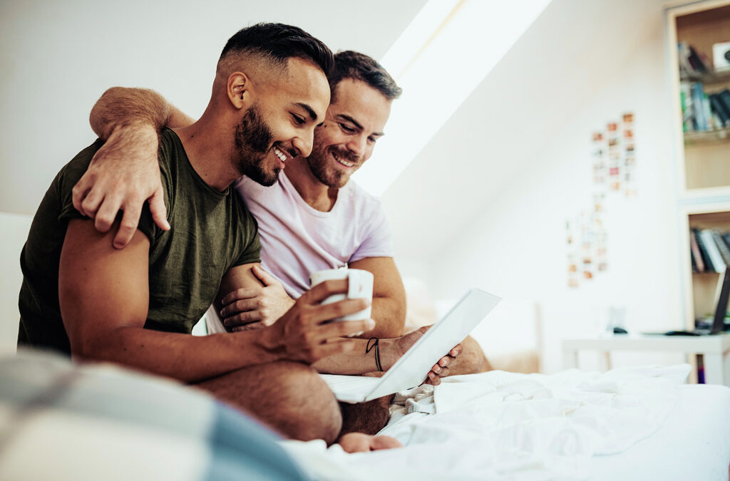 Two men smiling as they look at a shared laptop.