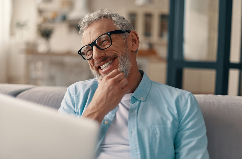 Man smiling broadly from behind a laptop.