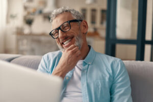 Man smiling broadly from behind a laptop.