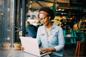 Focused young woman sitting alone at a counter in a cafe working on a laptop and listening to music on earphones
