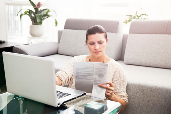 Woman looking at paper and laptop in front of couch