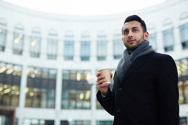 Young professional holding coffee outside of an office building